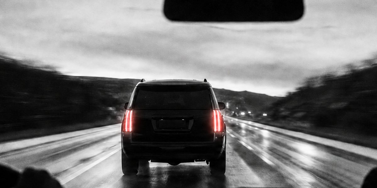 Armoured SUV and its follow car in a protected convoy on a wet road at dusk